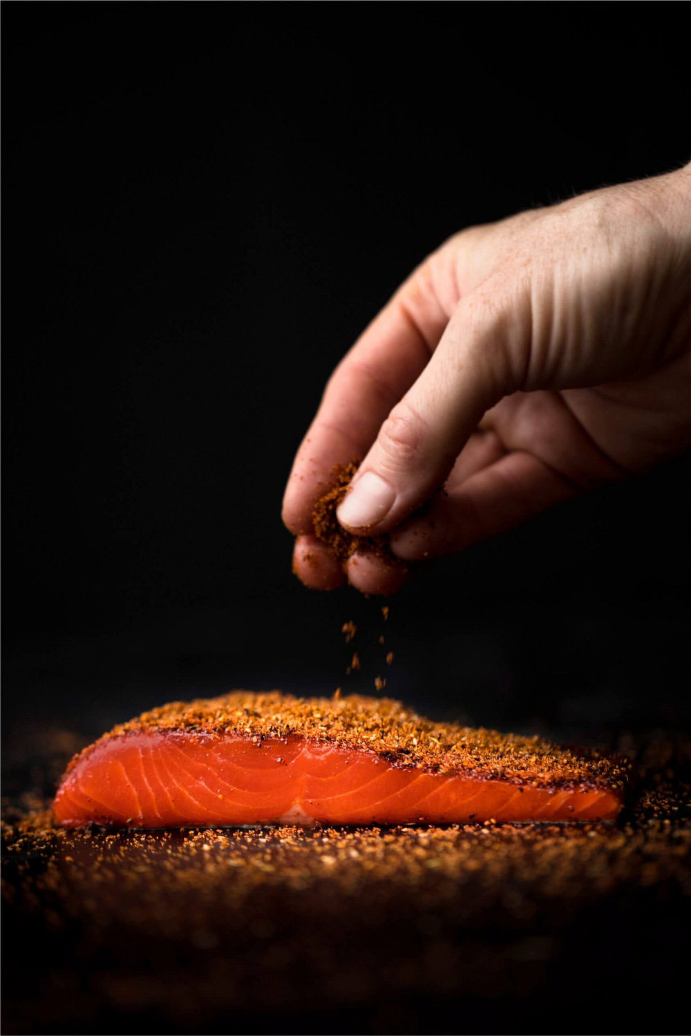 a hand sprinkling spices over a salmon steak