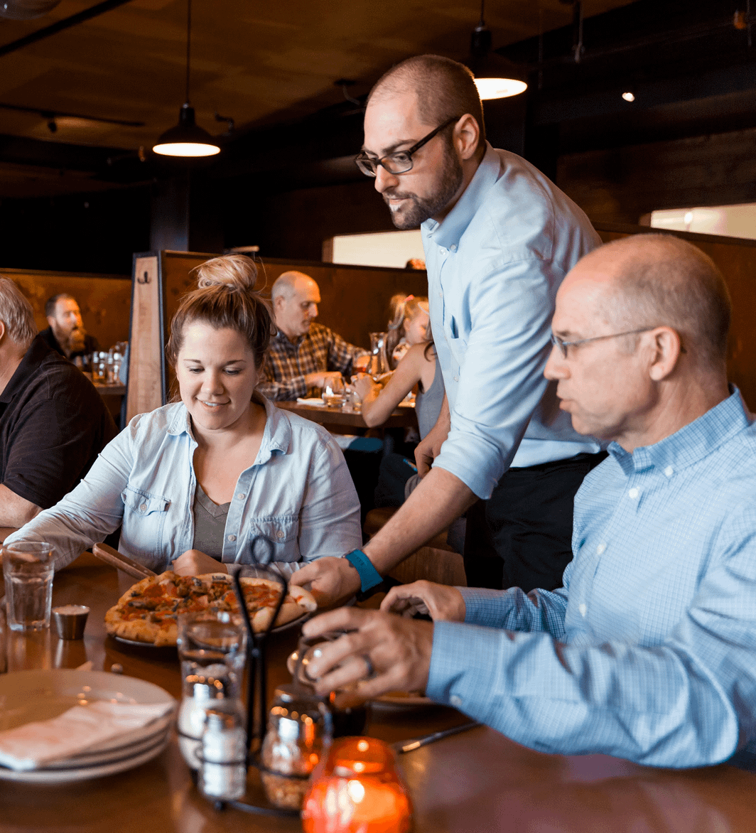 a waiter serves a pizza to two diners