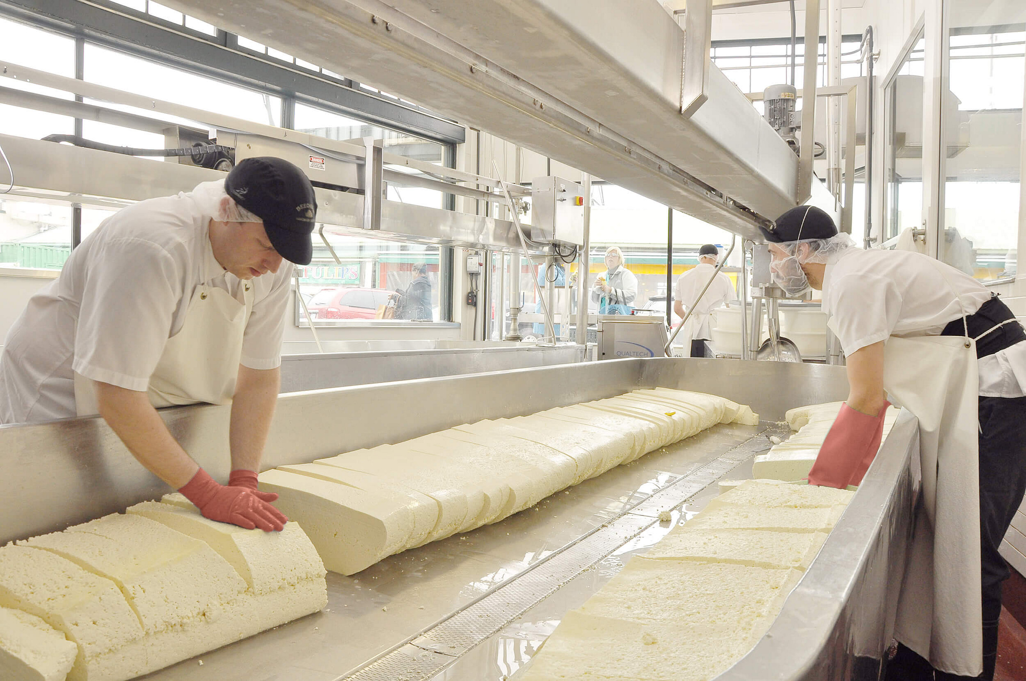 Two workers slice and stack bricks of cheese curds