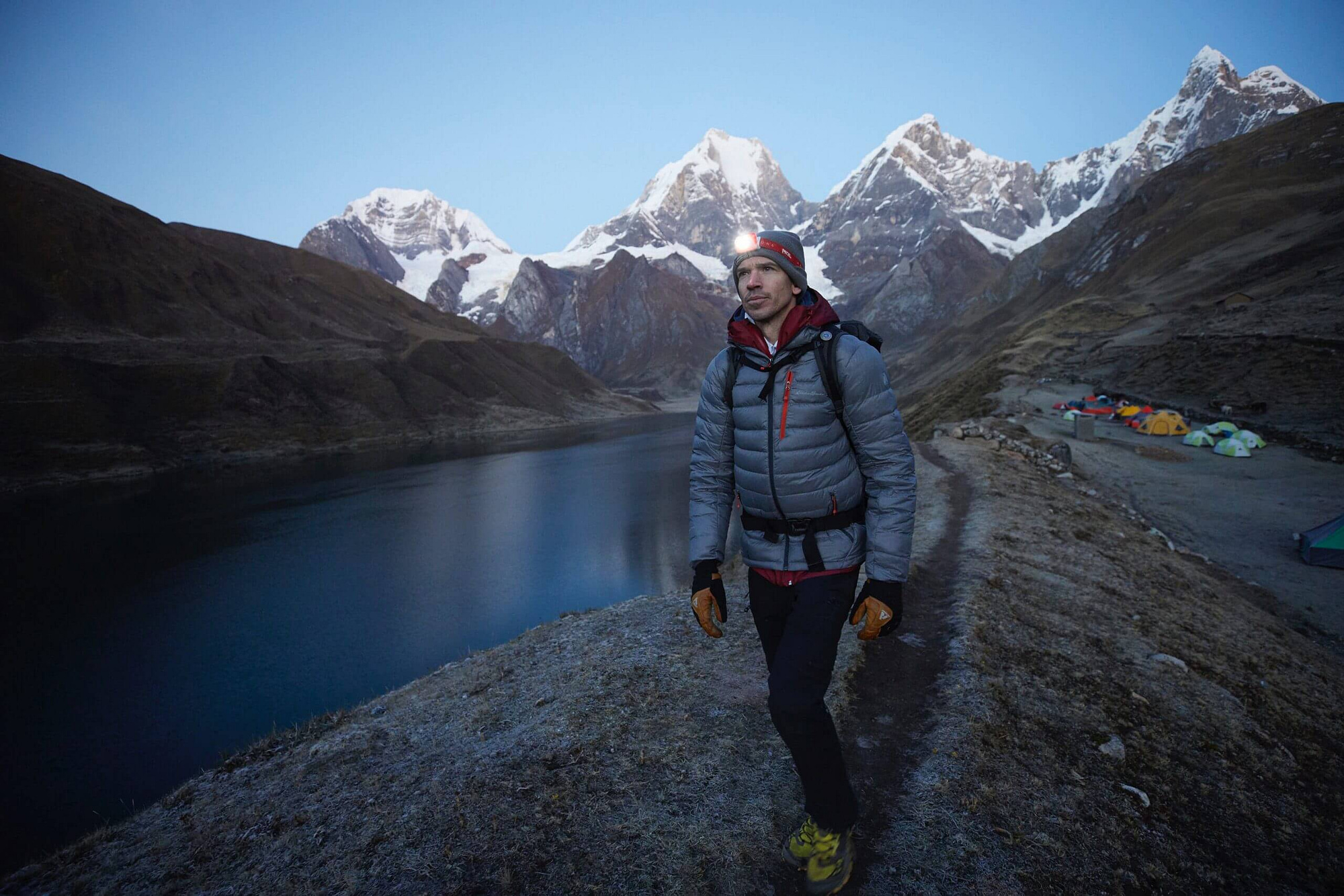 a male hiker with headlamps walks on a lakeside trail at dusk