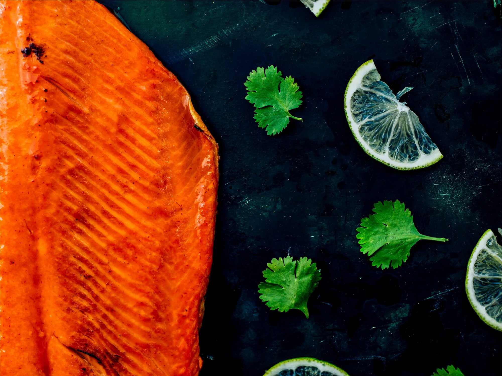 a fillet of cooked sockeye salmon laid out on a slate stone with cilantro leaves