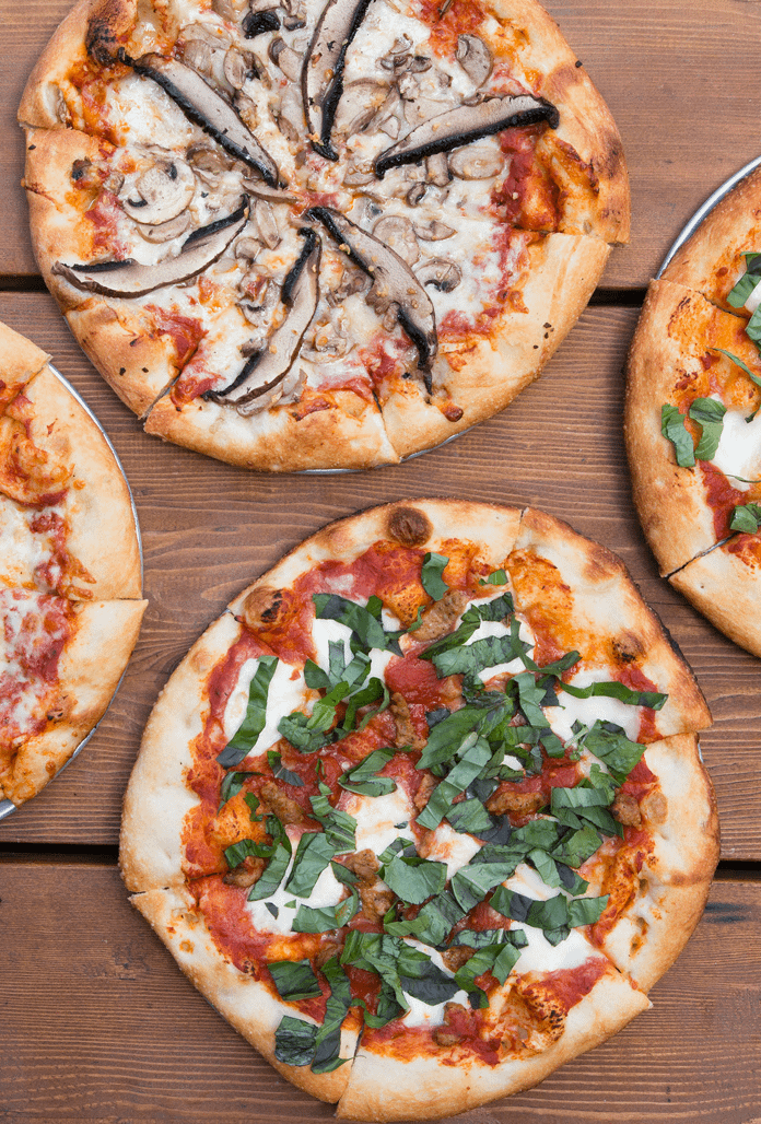 four delicious looking pizzas laid out on a wooden table