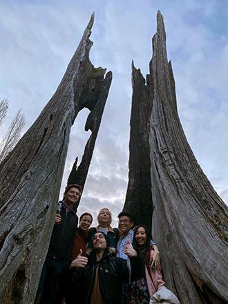 Mentor team posing inside a driftwood tree stump at the beach